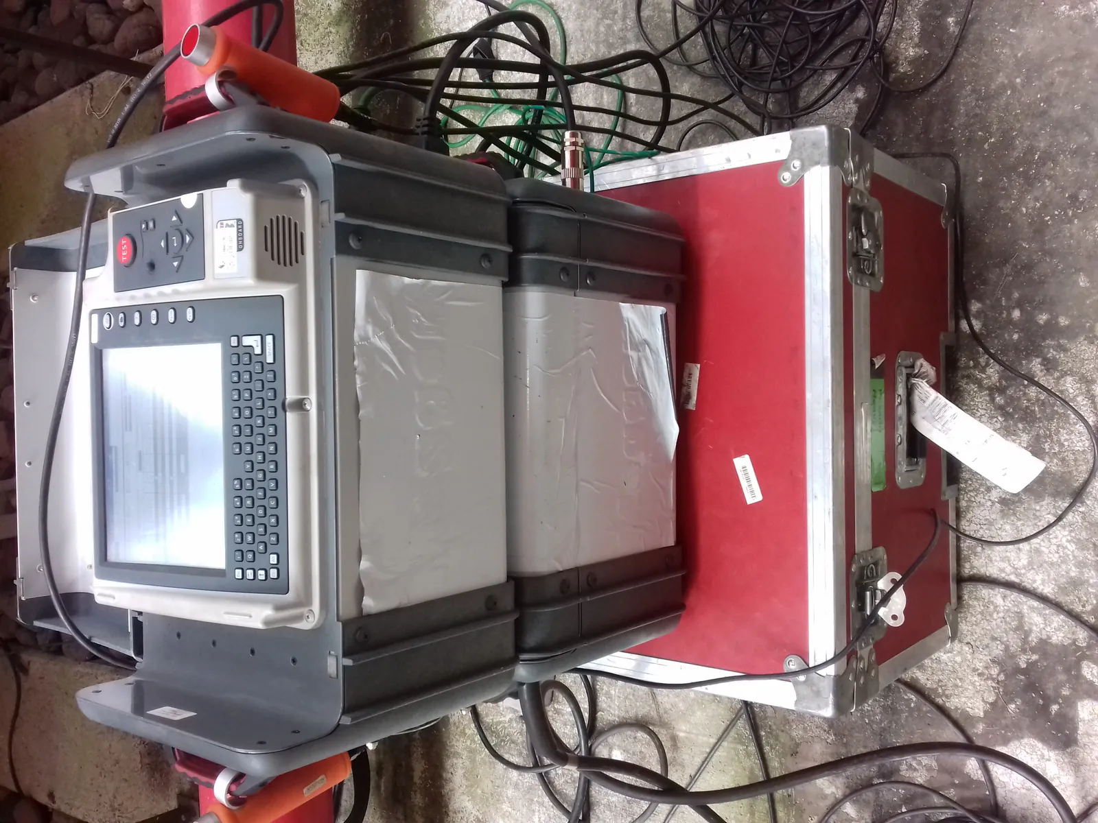 Equipo de prueba de factor de potencia abierto sobre su estuche de transporte, con los cables tendidos en el piso de la subestación