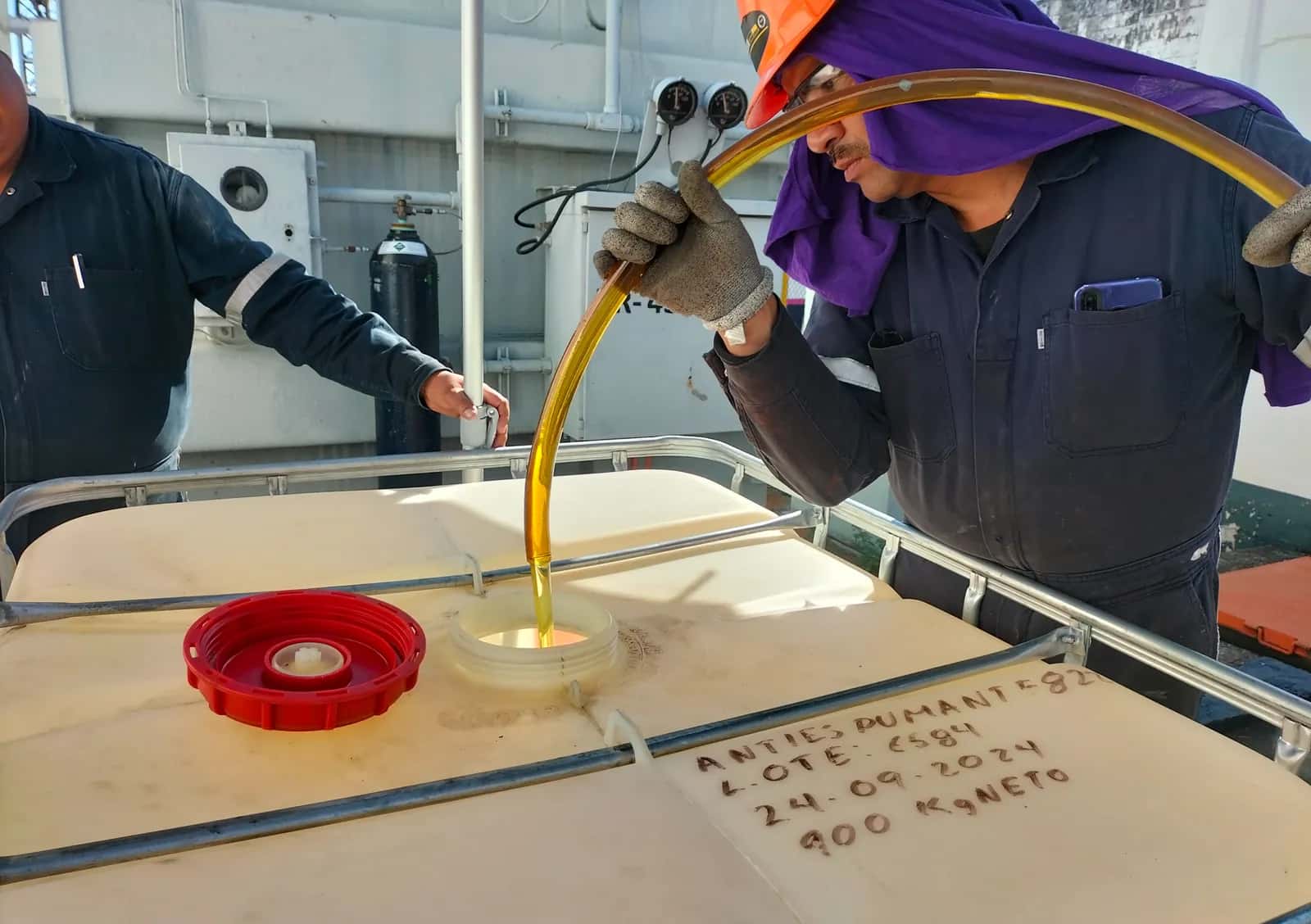Chorro de aceite dielectrico entrando por la boca de un depósito, guiado por un técnico con la manguera sobre la tapa
