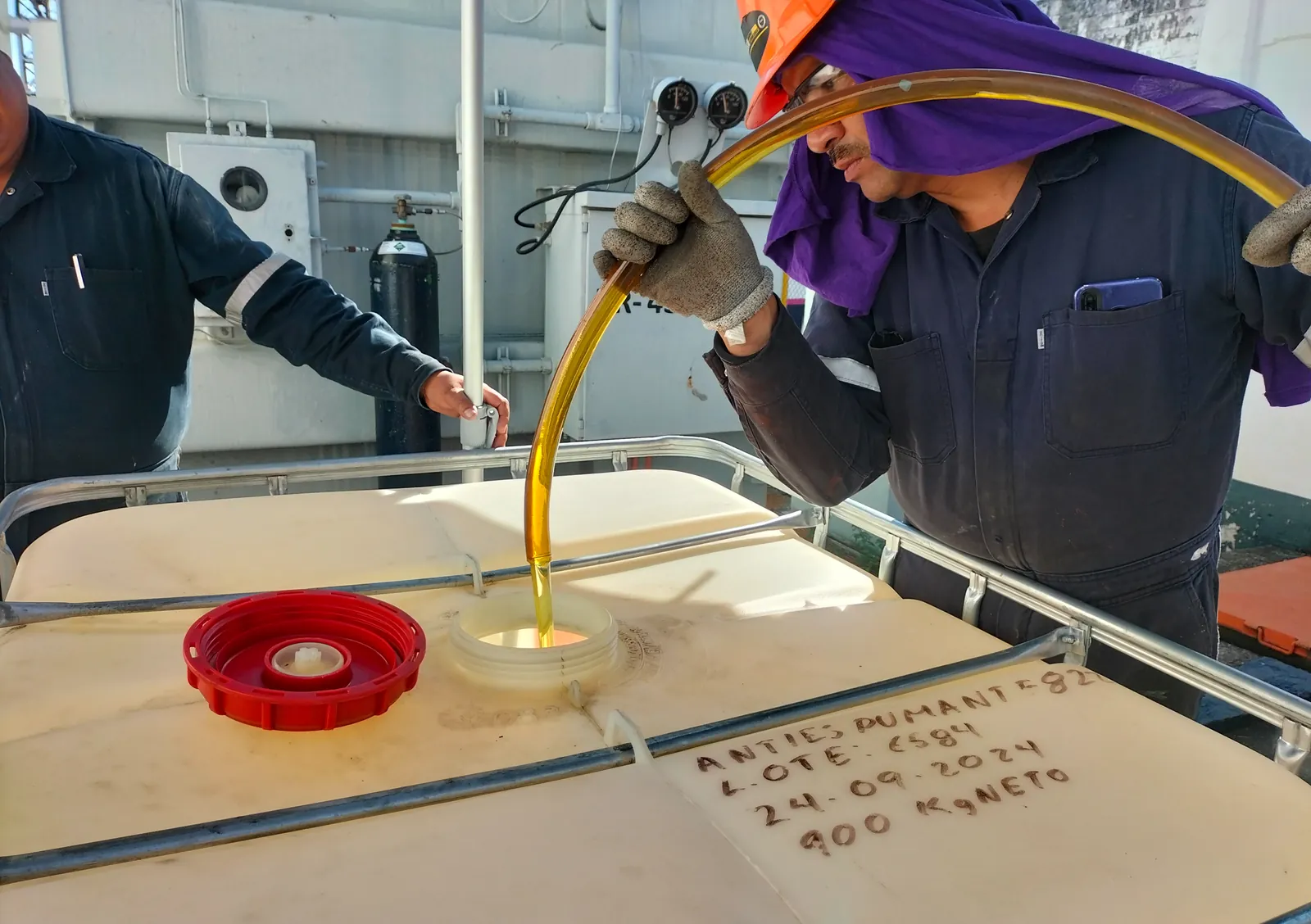 Chorro de aceite dielectrico entrando por la boca de un depósito, guiado por un técnico con la manguera sobre la tapa