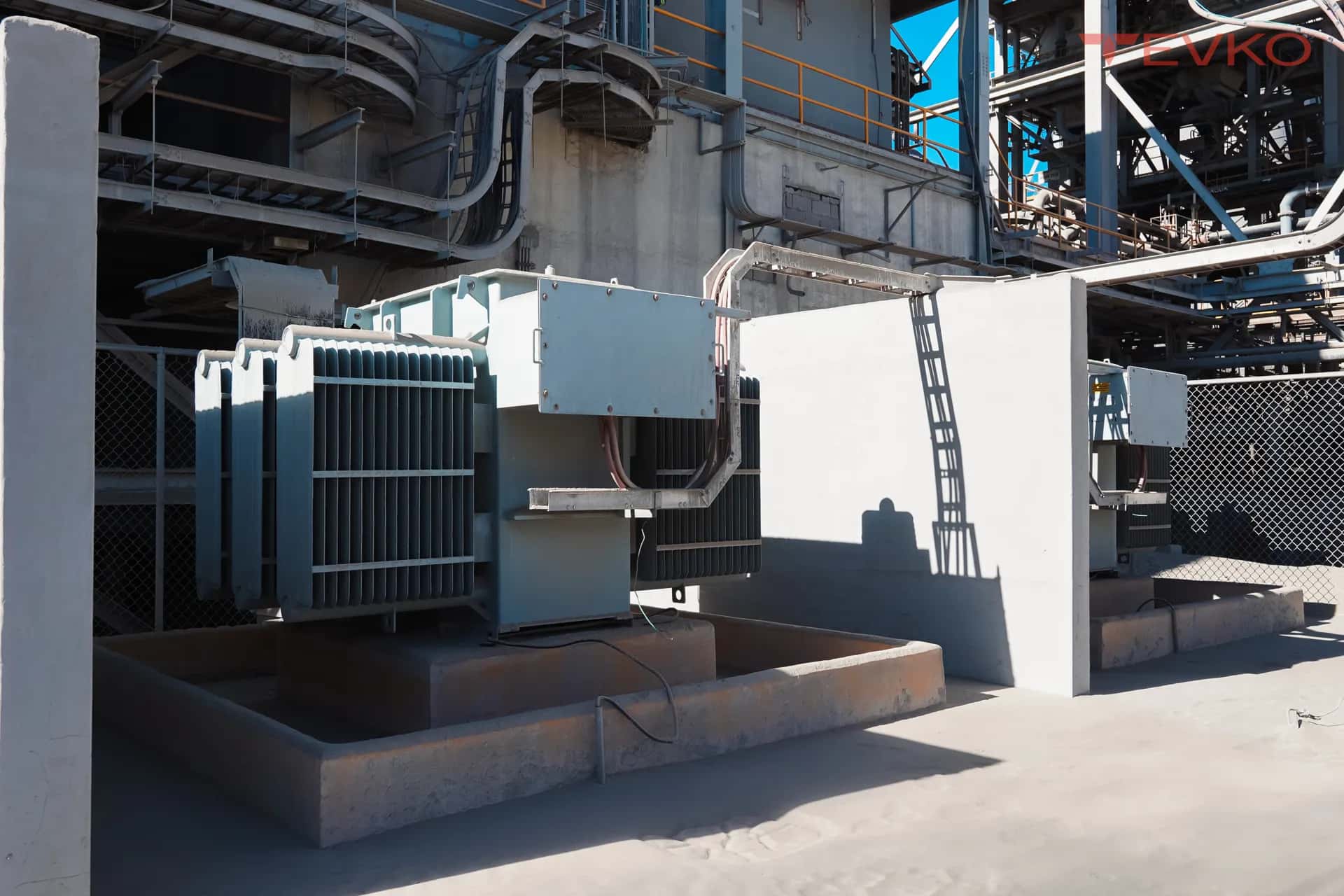 Transformador y gabinete sobre base de concreto junto a una estructura industrial