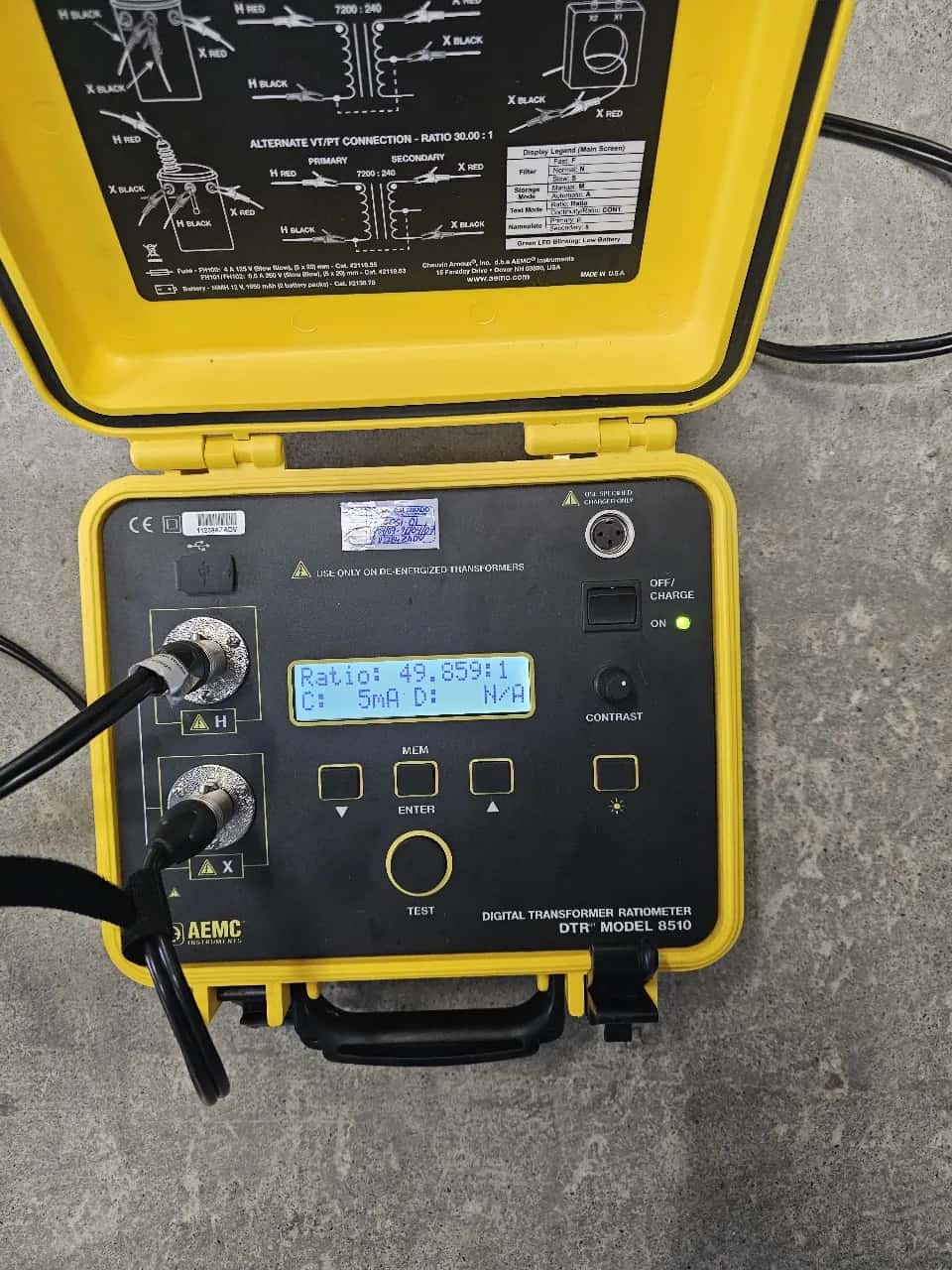 Digital transformer turns-ratio meter open in its yellow case, showing a ratio of 49.85 to 1 on screen