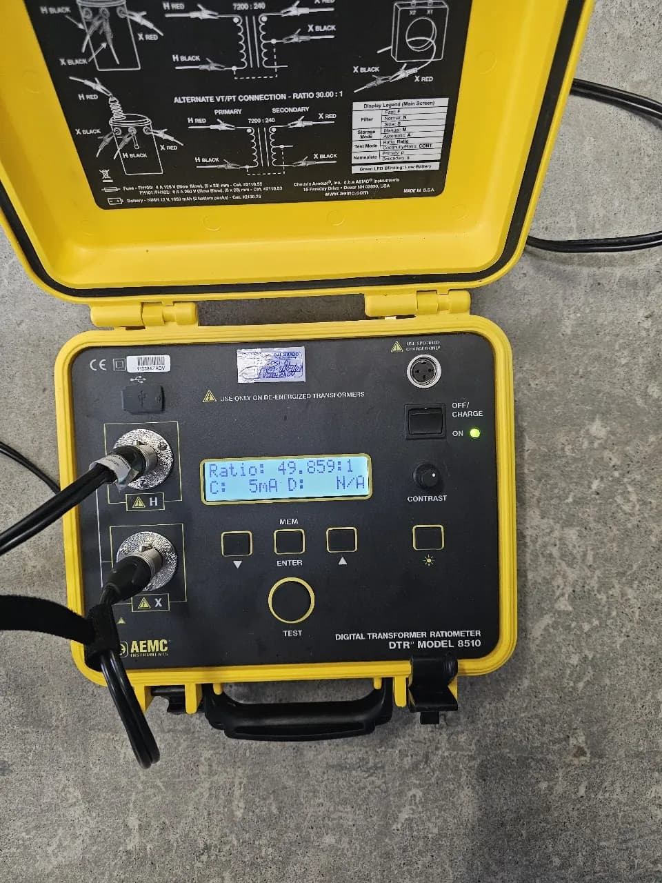 Medidor digital de relación de transformación abierto en su estuche amarillo, mostrando en pantalla una relación de 49.85 a 1