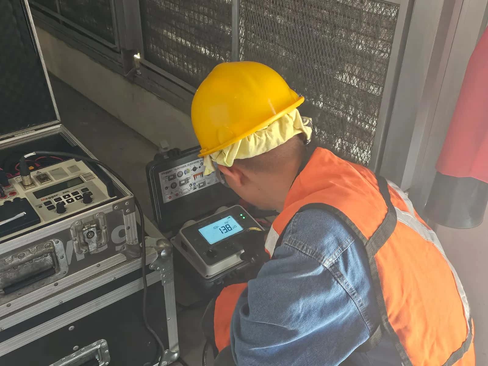 Técnico agachado operando dos instrumentos de prueba conectados entre sí, con los cables tendidos hacia el equipo