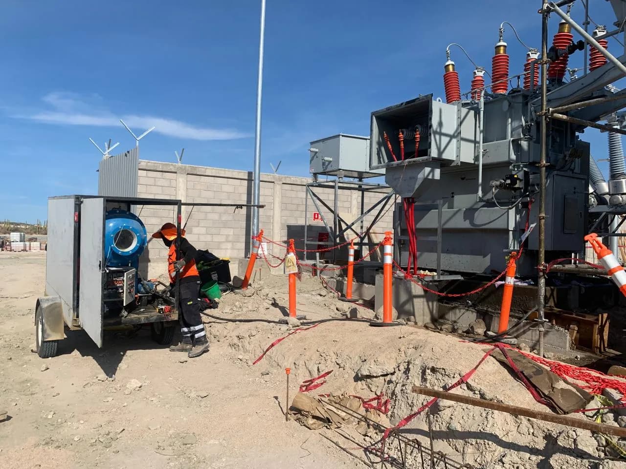 Técnico operando la planta de vacío junto a un transformador de potencia con boquillas rojas, en una subestación en construcción