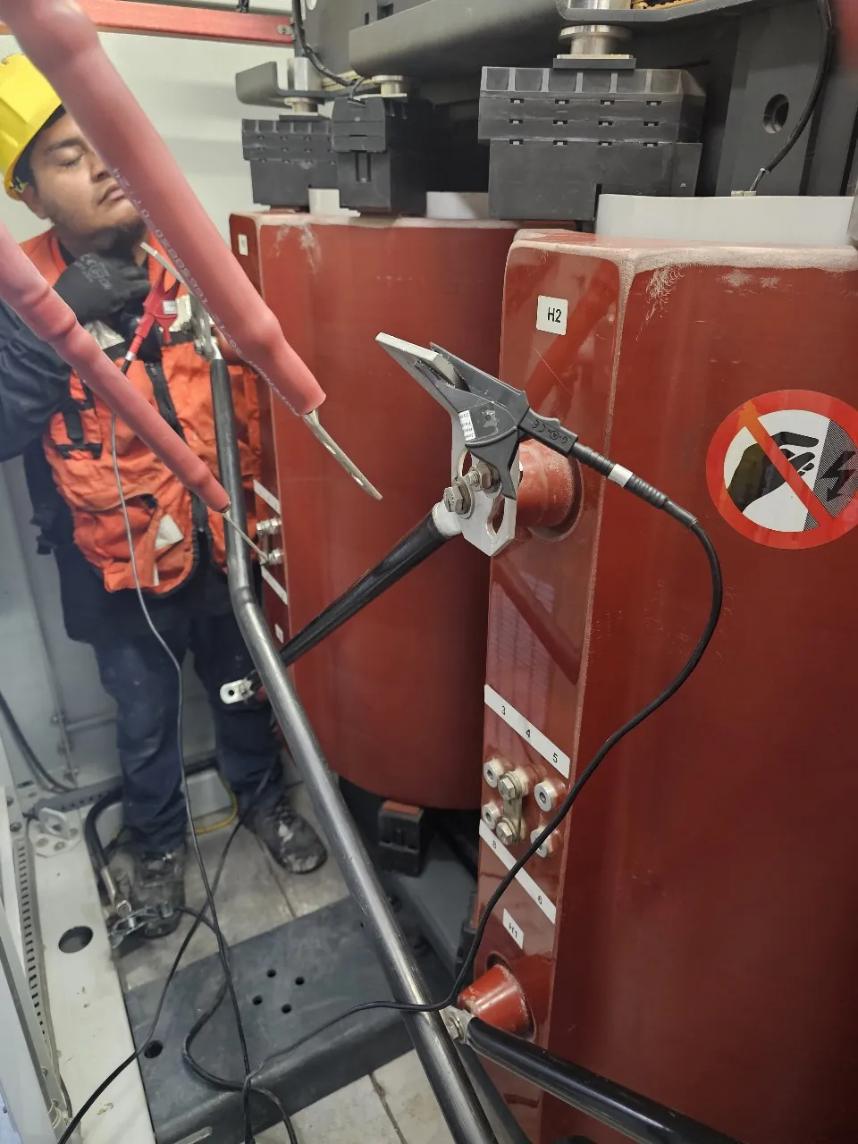 Pinza de prueba sujeta a la terminal H2 de un transformador seco, con el cable del instrumento tendido hacia el piso