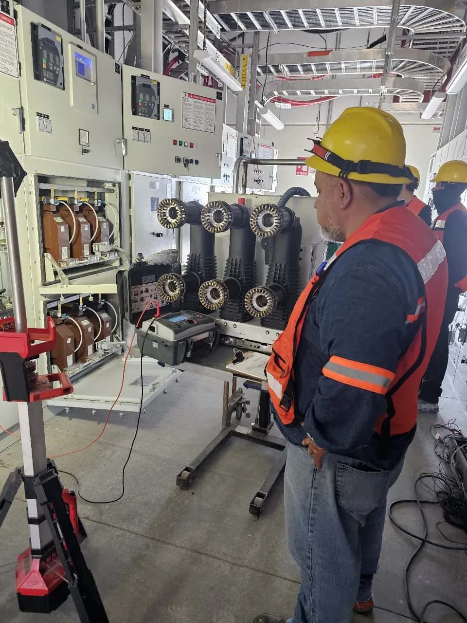 Sala de celdas de media tensión con las boquillas y los transformadores de corriente a la vista, y un técnico junto al equipo de prueba
