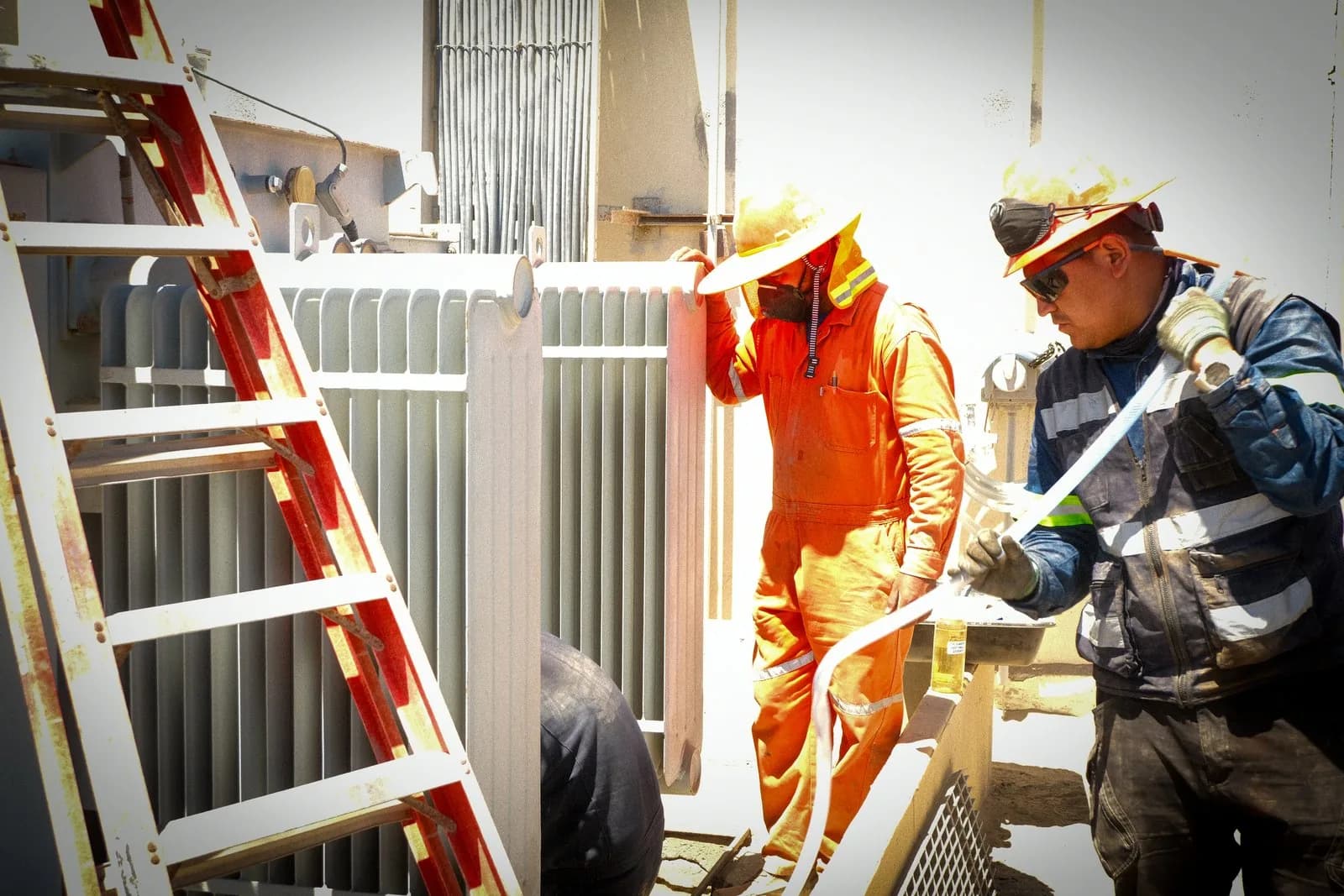Dos operarios trabajando en la válvula lateral de un transformador, con una escalera apoyada en el equipo