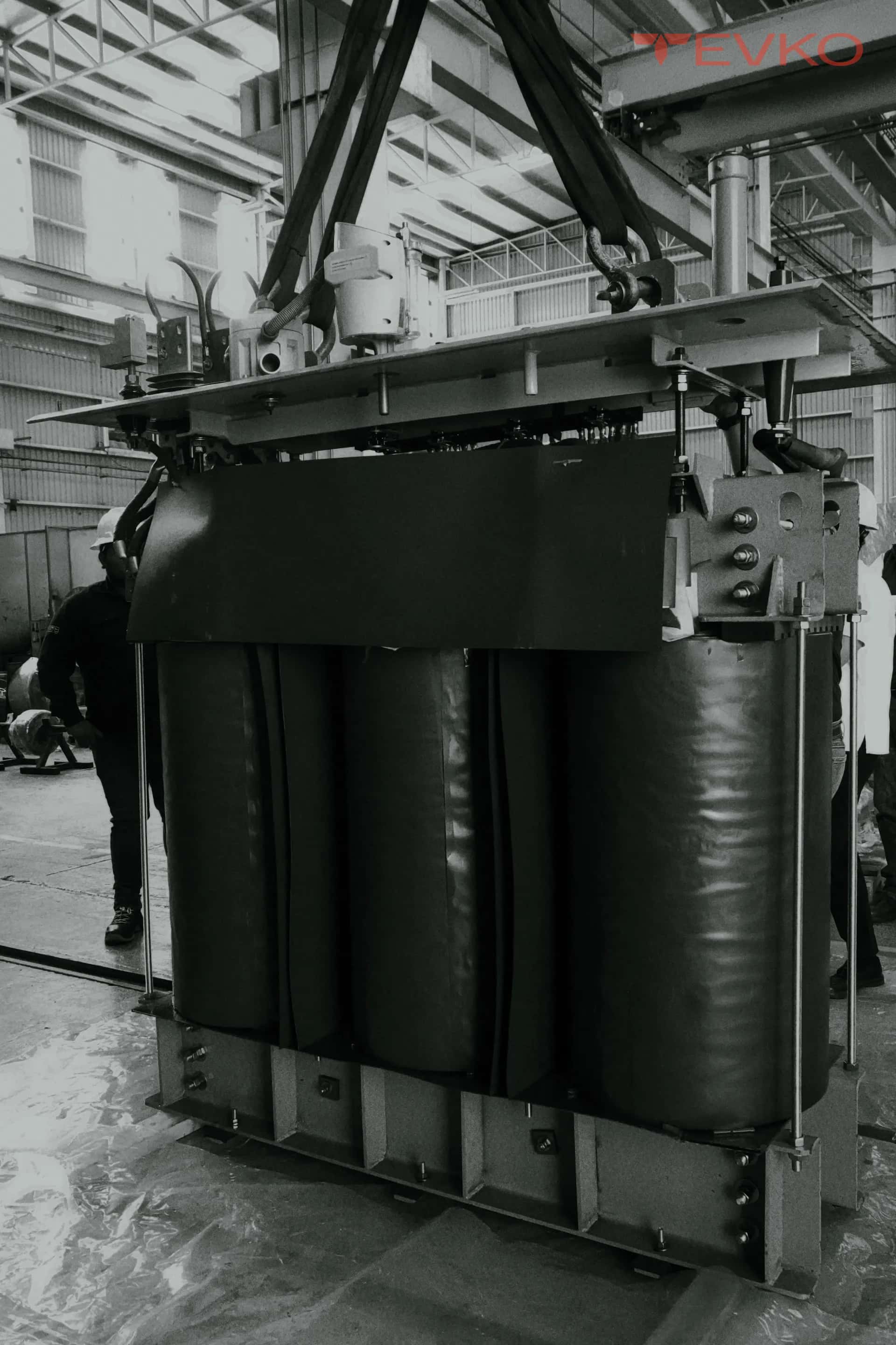 Parte activa de un transformador suspendida de una grúa dentro de la nave de taller, en blanco y negro