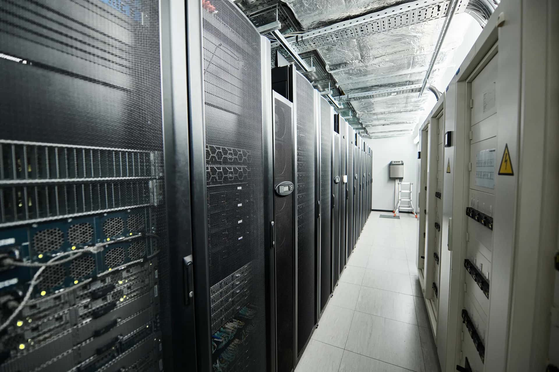 Pasillo de un centro de datos entre racks de servidores y tableros eléctricos.