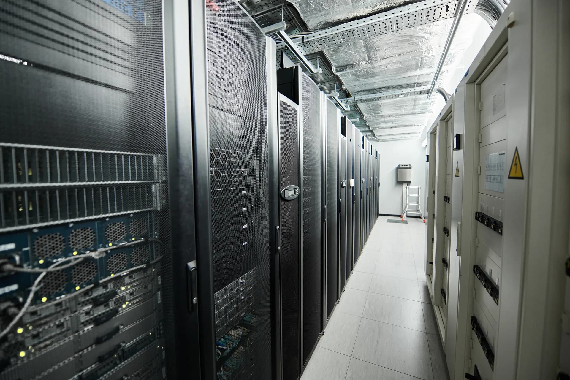 Pasillo de un centro de datos entre racks de servidores y tableros eléctricos.