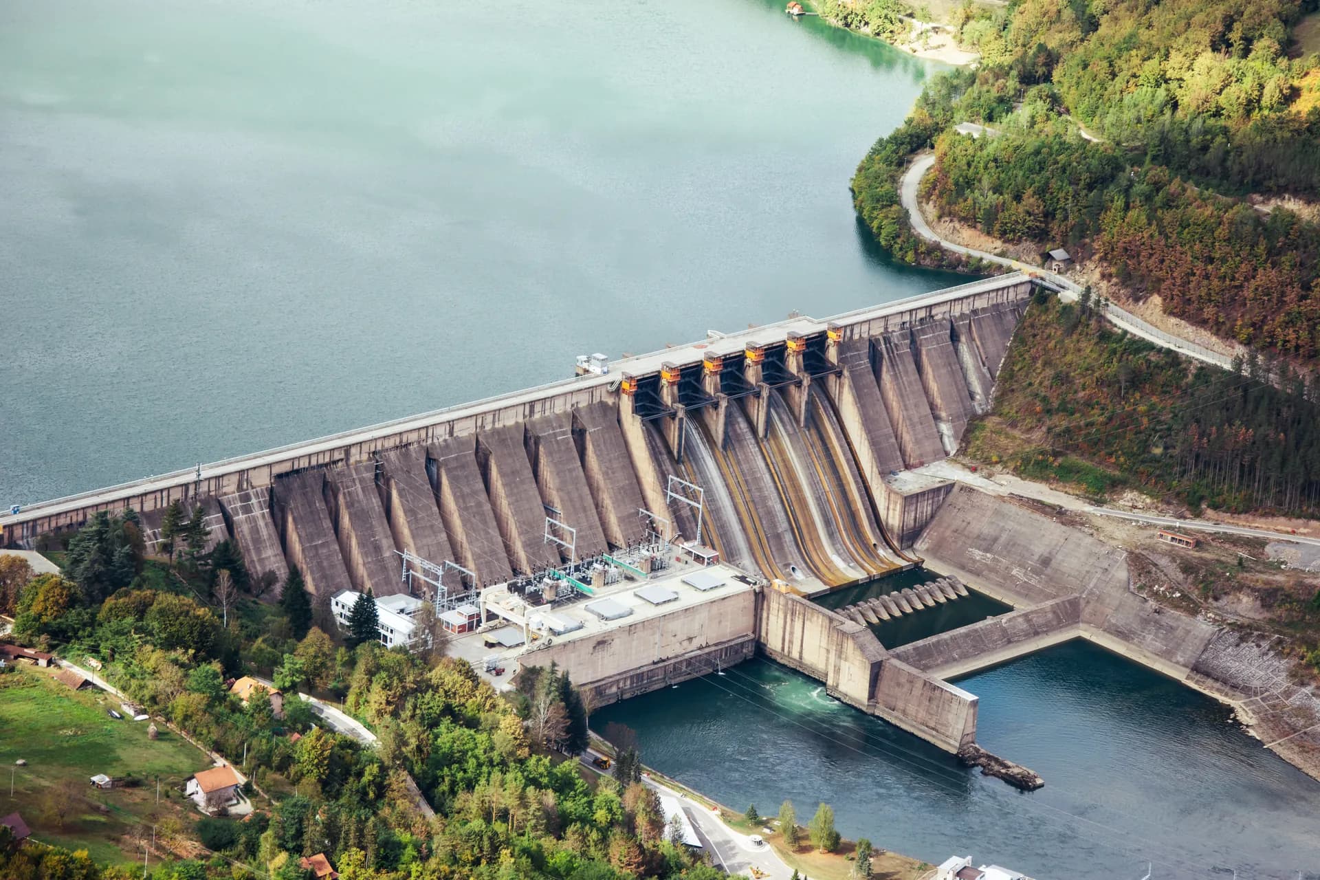 Cortina de una central hidroeléctrica vista desde el aire, con la casa de máquinas al pie y el embalse detrás.