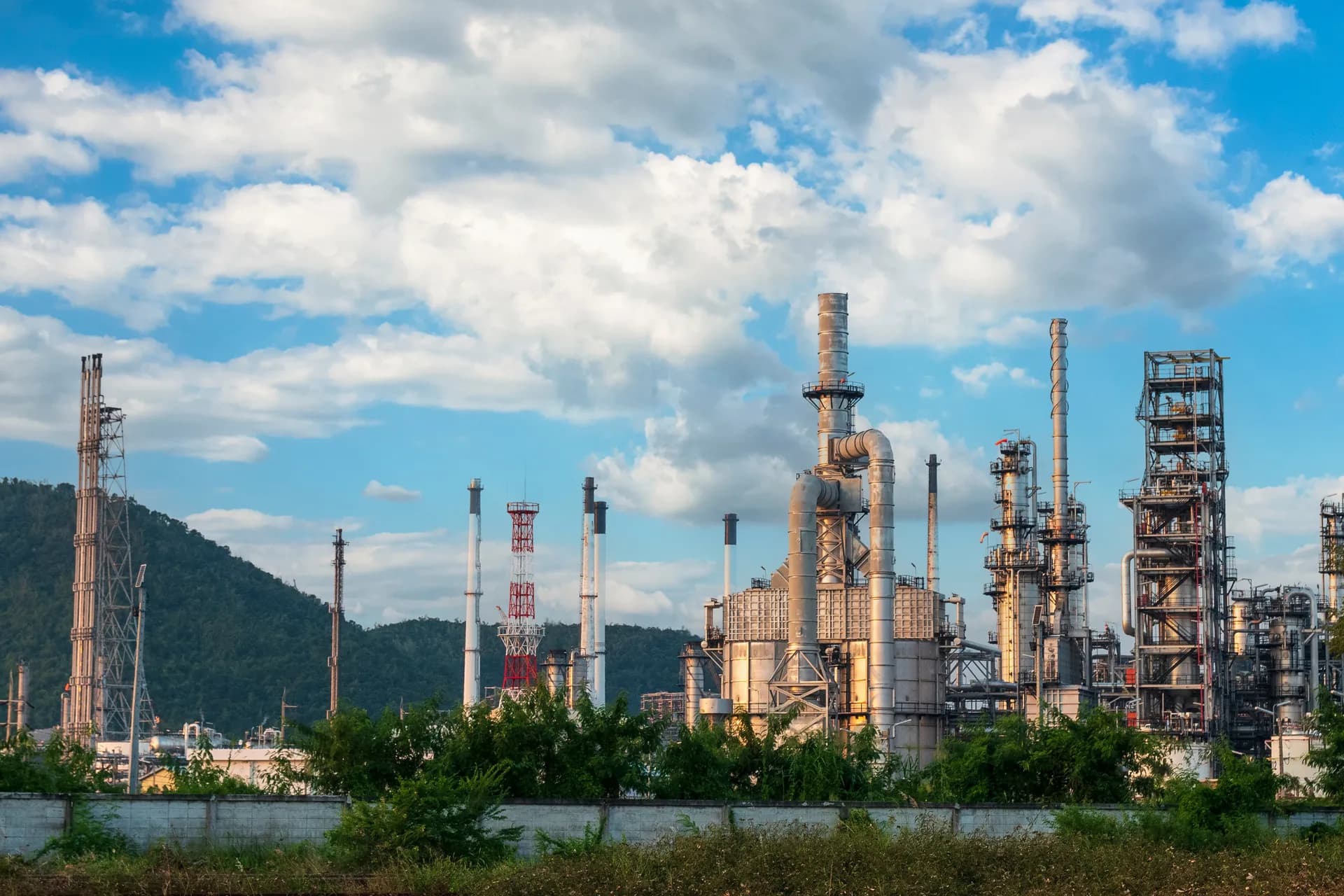 Refinería con torres de destilación, chimeneas y racks de tubería bajo cielo despejado.