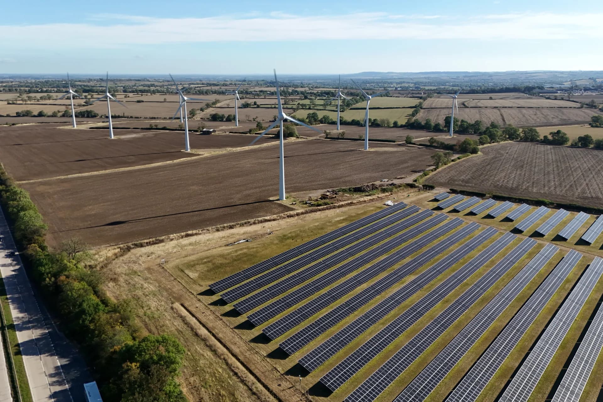 Vista aérea de un campo fotovoltaico junto a aerogeneradores sobre terreno de cultivo.